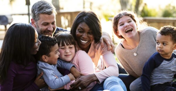 A multi-ethnic blended family at the park on a sunny day, sitting together on the ground on a blanket, laughing.